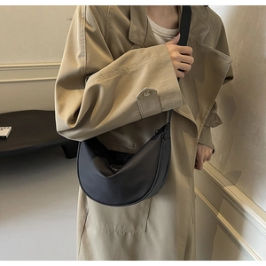 Détail d'un sac bandoulière noir en demi-lune porté avec un trench beige au look tendance