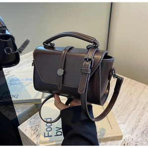 Close-up of a vintage dark brown leather crossbody bag on a marble table with books