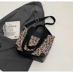 Detail of leopard print tote bag with black leather base on a grey blazer backdrop