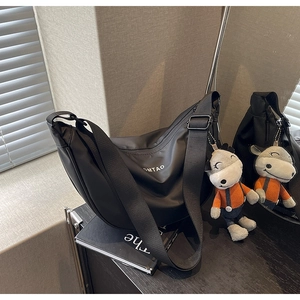 Détail d'un sac bandoulière noir en demi-lune avec logo et porte-clés peluche âne