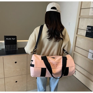Pink cylinder fitness bag with black straps worn by a model in a cozy home setting
