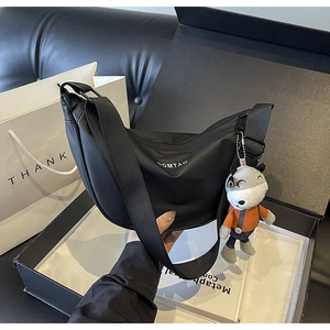 Vue détaillée d'un sac demi-lune en nylon noir avec bandoulière et peluche dans un coffret