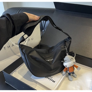 Détail du sac à bandoulière noir avec logo DOMTAO et charme en peluche vache cartoon
