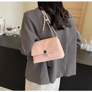 Dettaglio di una borsa rosa trapuntata con catena indossata su un blazer grigio