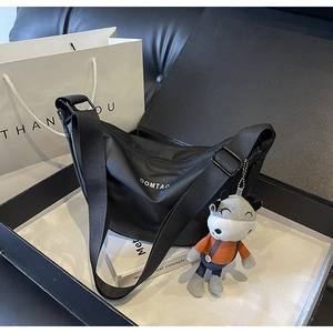 Détail du sac demi-lune en nylon noir avec logo OOMTAO et charm peluche vache mignon