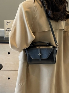 Minimalist black leather crossbody bag with silver buckle worn by a model in a trench coat