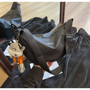 Détail du sac demi-lune en nylon noir avec bandoulière tissée et breloque en peluche