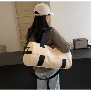 Detail view of beige canvas gym bag with black straps and elegant cursive embroidery