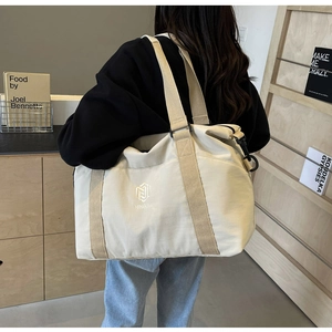 Vue arrière du mannequin portant un grand sac de voyage en toile beige à doubles poignées