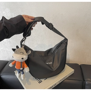 Détail du sac bandoulière croissant en nylon noir avec logo et pendentif vache en peluche