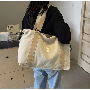 Détail d'un grand sac de voyage en toile beige avec logo brodé et bandoulière réglable
