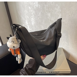 Détail du sac bandoulière croissant en nylon noir avec logo blanc et breloque en peluche