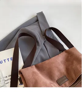 Close-up of brown suede tote bag featuring a brand logo tag and wide woven shoulder strap