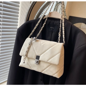 Dettaglio della borsa trapuntata color crema con catena d'argento su blazer nero elegante