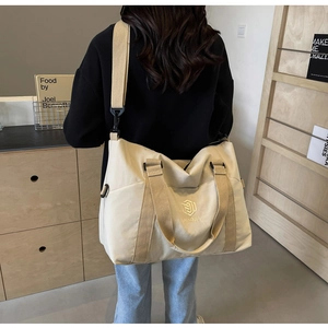Détail du sac de voyage en toile crème montrant la texture et le logo brodé