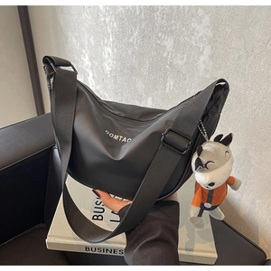 Détail du sac bandoulière croissant noir avec logo COMTAO et breloque peluche loup