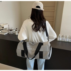 Grey canvas fitness bag with black straps worn by a model in a minimalist cafe