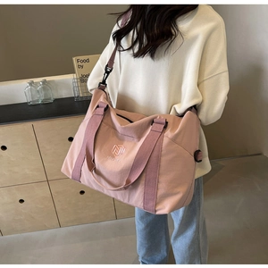 Détail d'un grand sac de voyage en nylon rose avec bandoulière porté par un mannequin