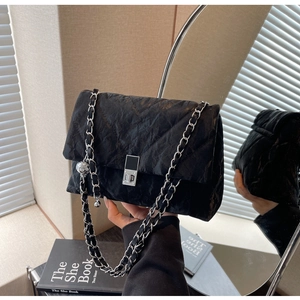 Detail of black quilted crossbody bag featuring silver chain strap and metal ball charm