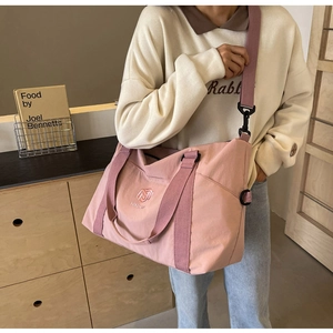 Gros plan du grand sac de voyage rose avec broderie de marque et bandoulière réglable