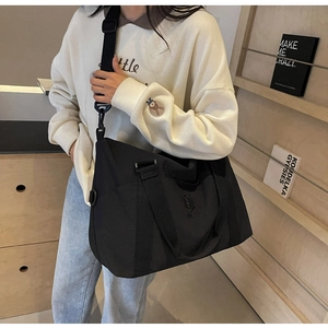 Vue détaillée du grand sac à bandoulière en nylon noir porté par un mannequin en intérieur