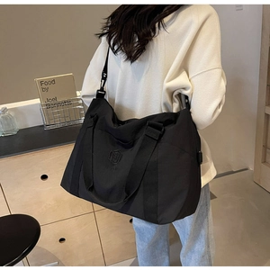 Grand sac de voyage noir avec logo brodé et bandoulière réglable porté par un mannequin