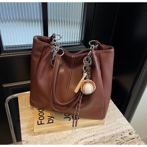 Detalle del bolso tote de cuero marrón oscuro con costuras blancas y adorno de béisbol