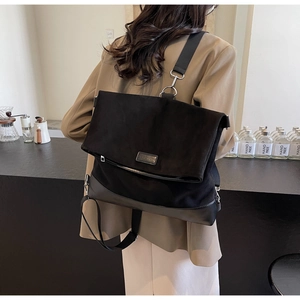 Side view of large black canvas messenger bag worn by model in a modern interior setting