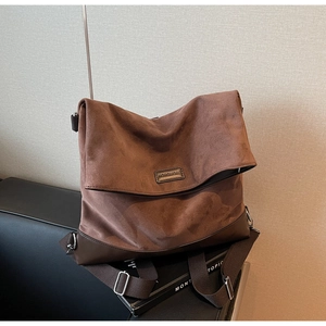 Close-up of vintage brown suede shoulder bag with metallic logo and wide fabric strap