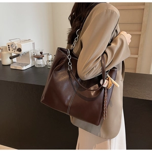 Detalle del bolso tote de cuero marrón oscuro con pespuntes blancos y colgante