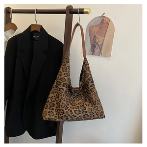 Close-up of leopard print tote bag hanging on wooden hanger with brown leather strap