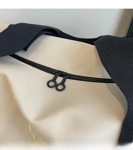 Dettaglio delle cerniere nere a due vie sulla borsa in tela color bianco sporco