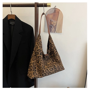 Close-up of leopard print tote bag with brown leather straps hanging in a minimalist setting