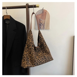 Detailed view of leopard print tote bag with brown straps hanging on a wooden hanger