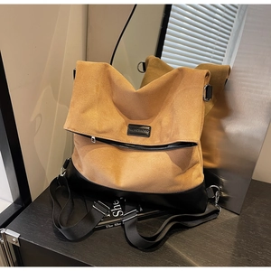 Detail of two-tone brown suede tote bag with black leather base on a vintage wooden surface