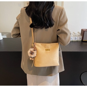 Detail of light yellow suede bucket bag with gold clasp and plush charm on shoulder