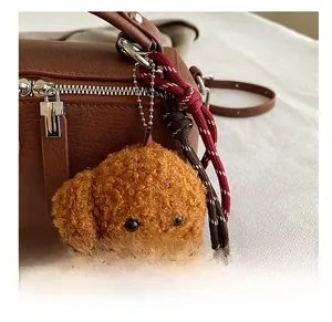 Gros plan d'une breloque caniche en peluche sur un sac en cuir marron avec bandoulière