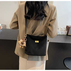 Detail of a black minimalist crossbody bag with a gold clasp and brown plush charm
