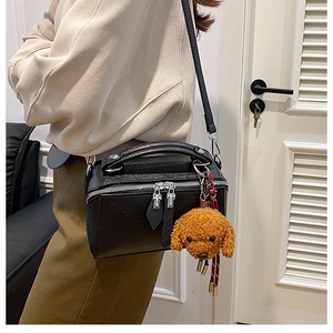 Détail du sac polochon en cuir grainé noir avec un charmant chien en peluche marron