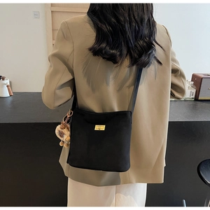 Detail of black crossbody bucket bag with gold lock and plush bear on a model