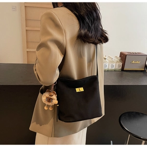 Detail showing matte black crossbody bag with gold twist lock and brown plush charm
