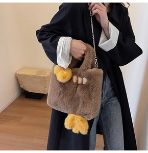 Gros plan sur un sac cabas en peluche marron avec pompon jaune et bandoulière chaîne