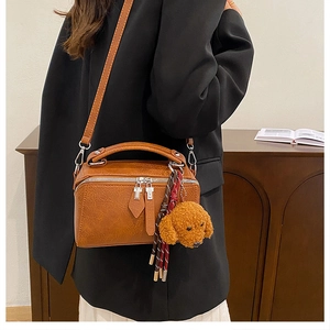 Détail du sac polochon marron avec breloque chien en peluche et pompon