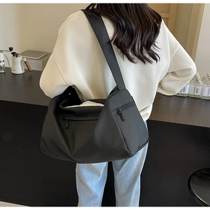Detail of a large black nylon crossbody travel bag featuring multiple zipper pockets