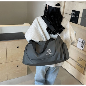 Detail of grey travel bag side pocket and logo carried by model in casual setting