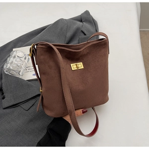 Detail of the golden metal turn-lock closure on a dark brown suede bucket bag