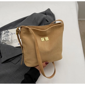 Detailed close-up of a camel suede shoulder bag featuring a gold metal twist lock