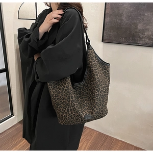 Detailed view of large leopard print tote bag with black leather straps on a black coat
