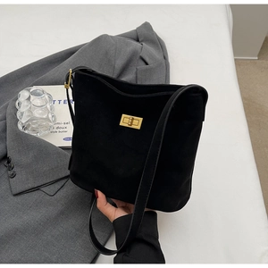 Detail of a matte black suede tote bag with a gold rectangular twist lock on a grey suit