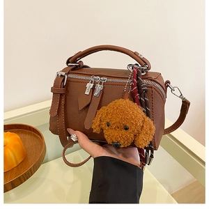 Détail d'un sac oreiller en cuir marron avec breloque ours en peluche et nœud tressé